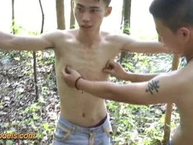 A captivating Asian boy finds himself bound in the woods, his hands behind his back. Amidst the rustling leaves and swaying trees, he's skillfully stroked to a climactic release. A bondage encounter in nature.